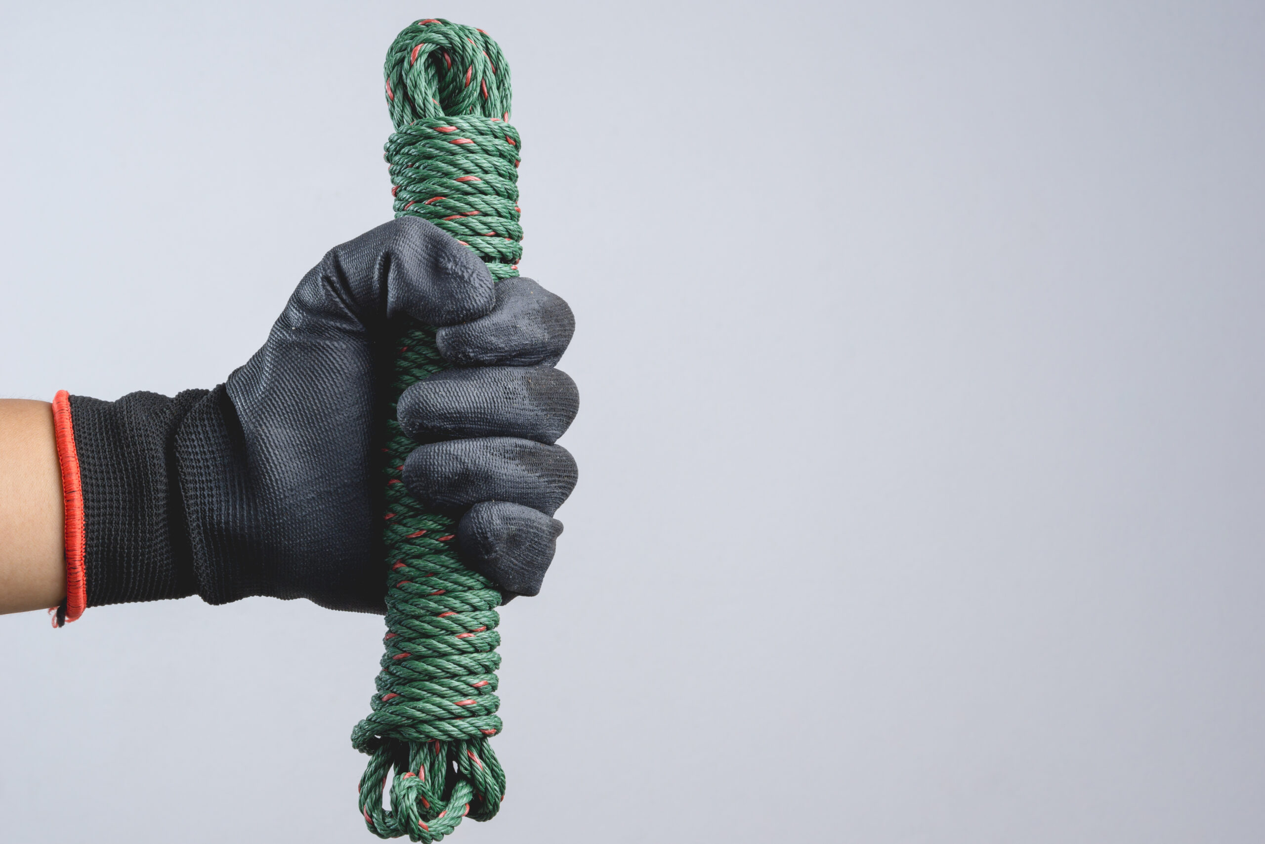 Hand wearing dark glove and holding green parachute cord of nylon rope as a kidnapper